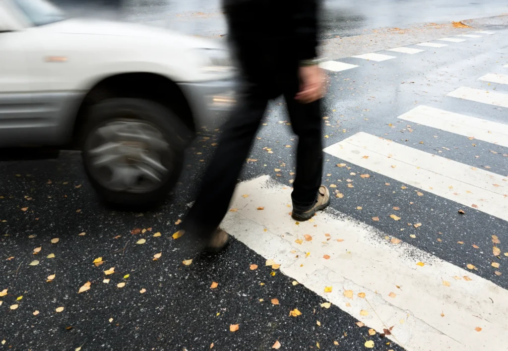 A pedestrian crossing at a crosswalk and a car incoming.