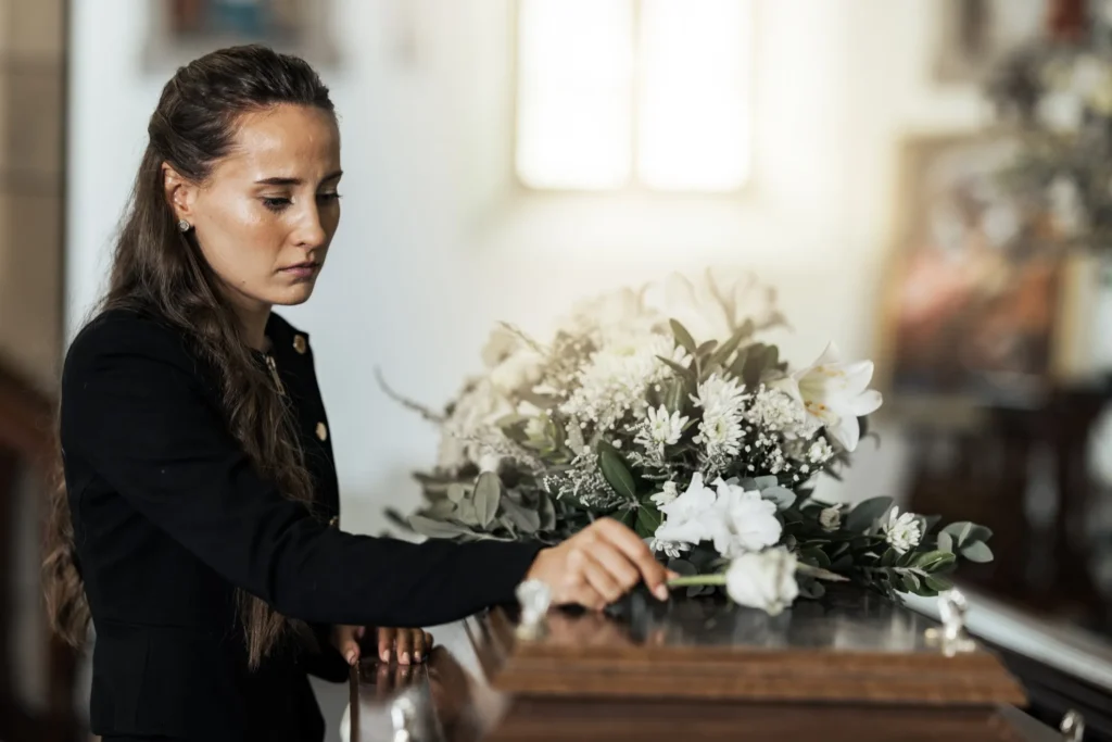 A woman standing at a casket mourning a loved one's death.