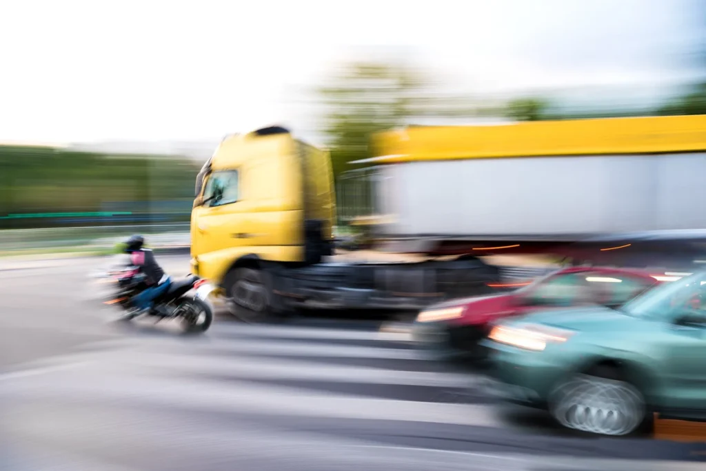 A motorcycle rider about to get hit by a large commercial truck.