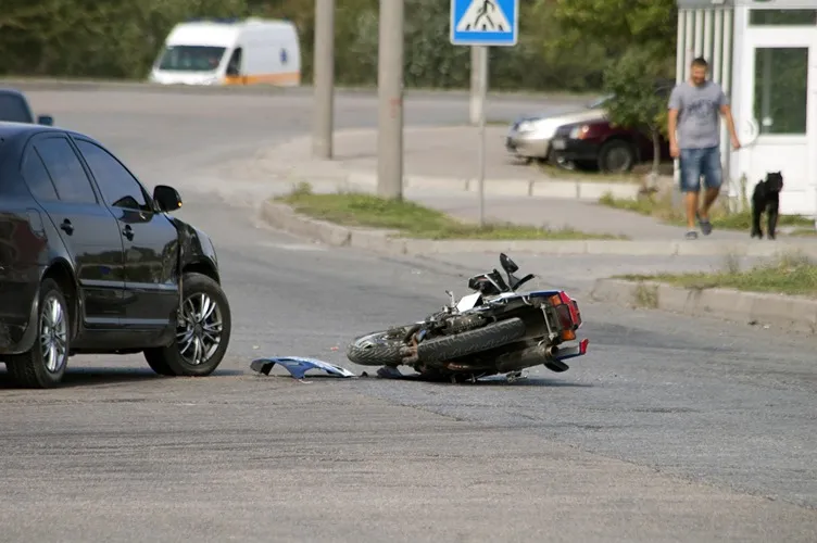 Crashed motorcycle on the street next to a car.