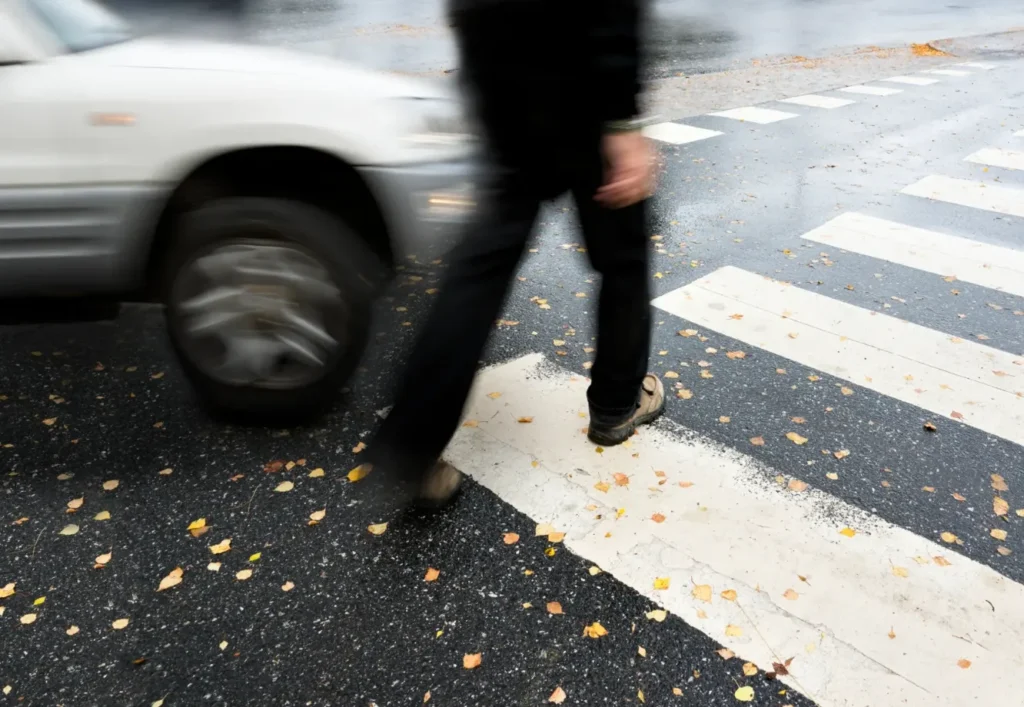 A pedestrian walking in a crosswalk with a car coming toward him.